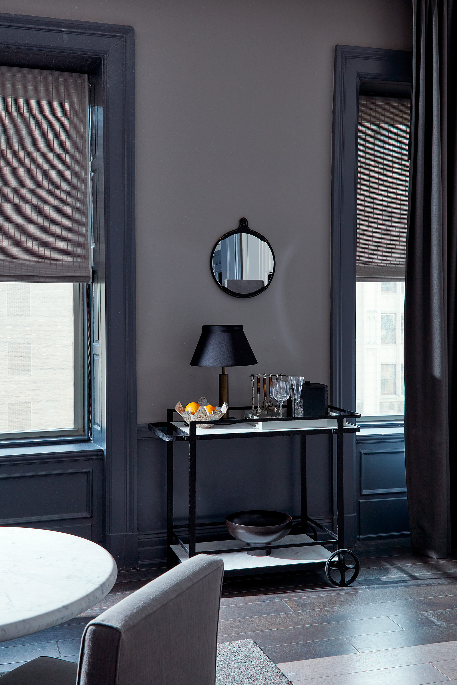 A bar cart situated between two windows with the blinds drawn halfway down.