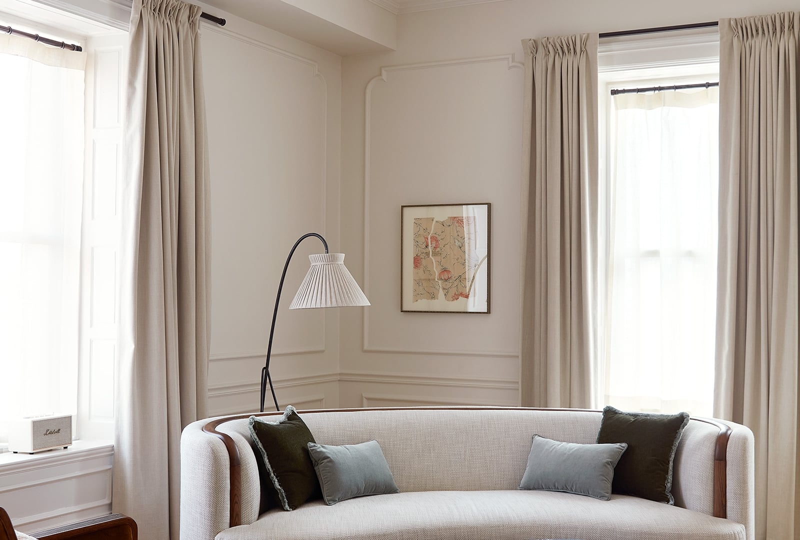 A white walled living room with wall moldings and a fireplace. There is a curved sofa and armchair with a reading lamp behind.