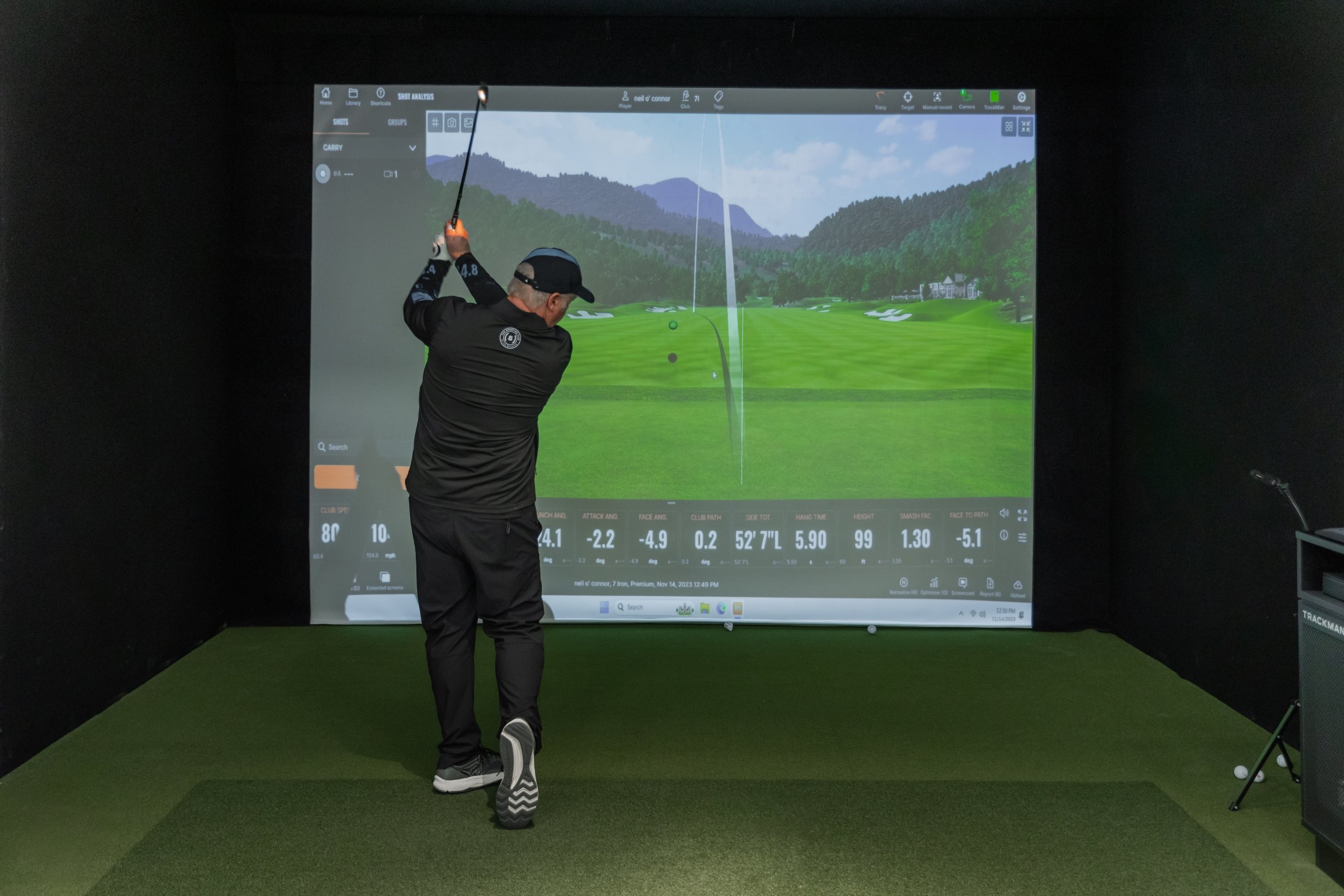 A man golfing in front of the golf simulator
