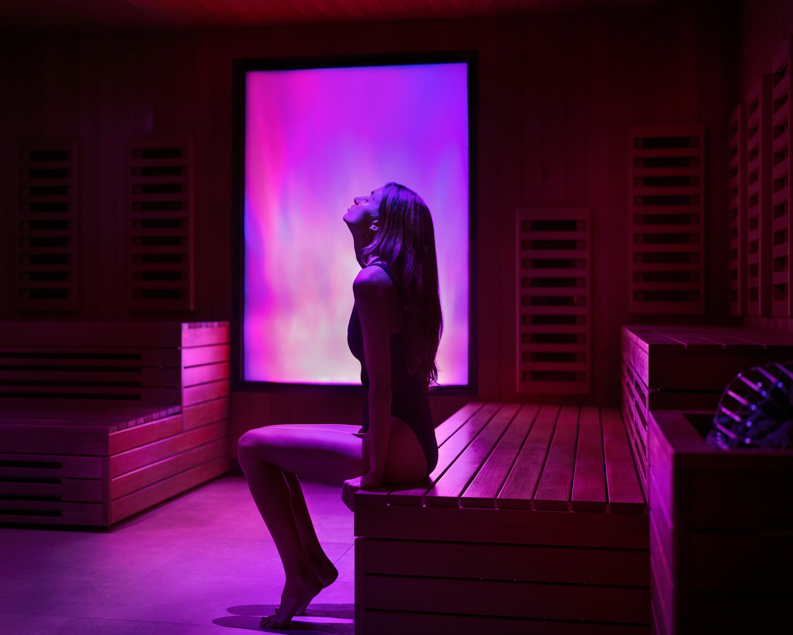 Women sitting on bench in sauna with purple lighting
